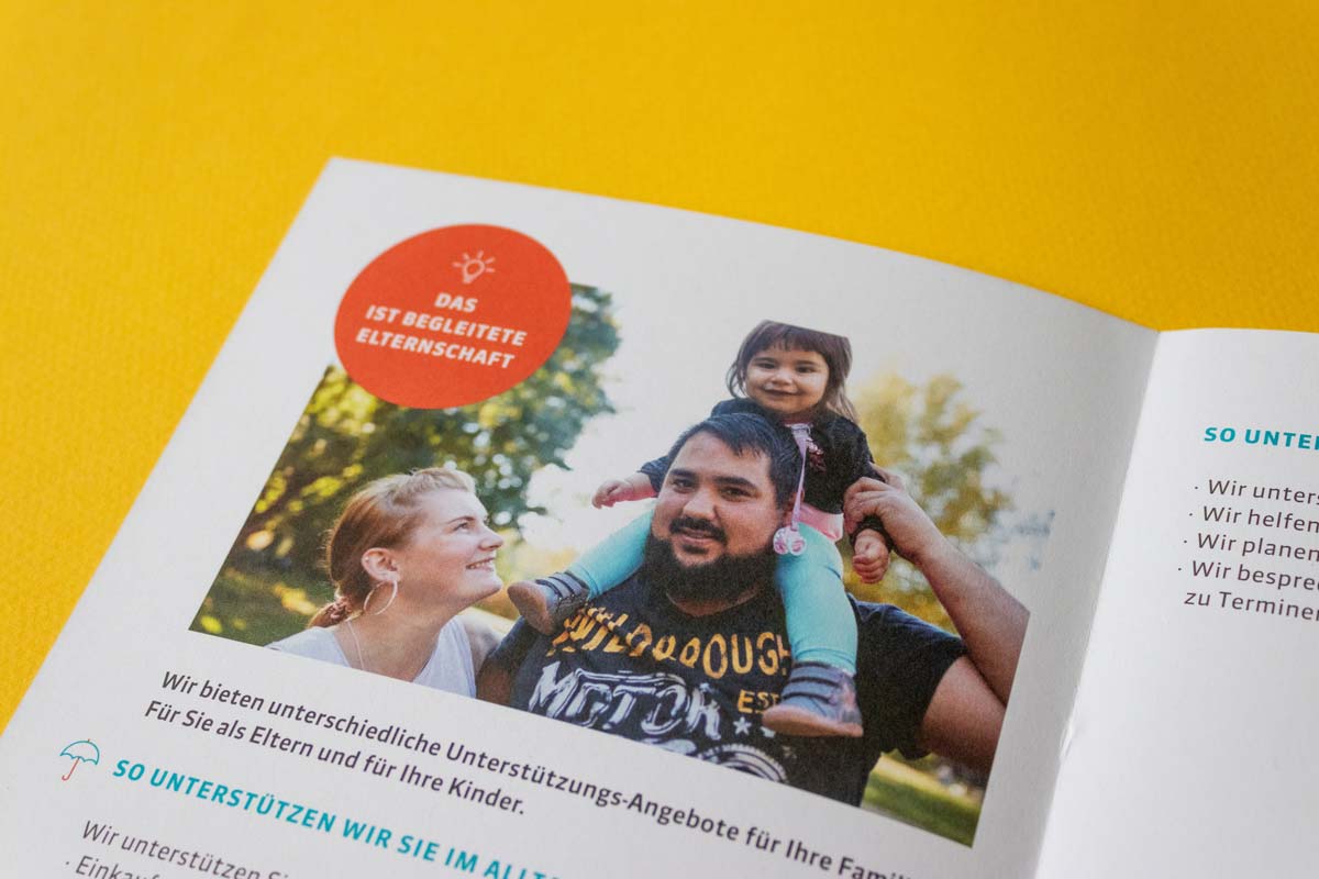 Aufgeschlagener Flyer „Begleitete Elternschaft“ zeigt das Bild einer Familie in einem Park